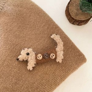 Détail d'une pince à cheveux en forme de chien tricoté marron avec des boutons décoratifs