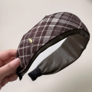 Macro detail of brown plaid woolen headband with a gold Love engraved metal tag