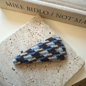 Détail d'une pince à cheveux tricotée à carreaux bleus sur un support en pierre