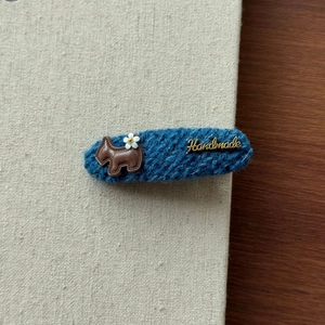 Détail de la pince BB en tricot bleu foncé avec motif chiot marron et étiquette Handmade