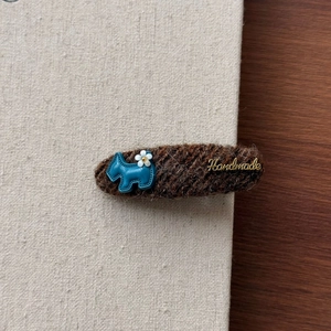 Détail de la pince à cheveux en maille marron avec petit chien bleu et étiquette dorée