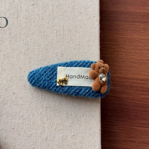 Détail de la barrette en tricot bleu avec un petit ours floqué et un nœud doré chic