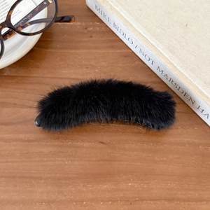 Detaillierte Nahaufnahme einer schwarzen Kunstpelz-Haarklammer auf einem Holztisch