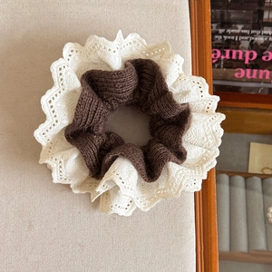 Brown knitted scrunchie with white floral lace trim on beige linen tray background