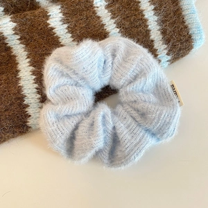 Makroaufnahme von hellblauem Strick-Scrunchie mit weicher Textur und Markenlabel