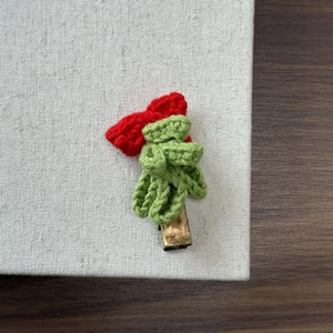 Detail of a handmade knitted Christmas hair clip with a red bow on a textured background
