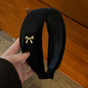 Detail view of a thick black velvet headband featuring a delicate golden bow accessory