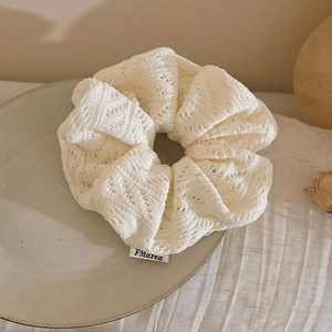 Detail of soft white knitted scrunchie with scalloped edges and minimalist brand label