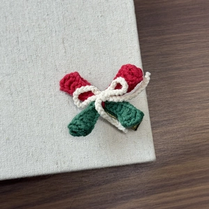 Detail of red and green hand-knitted Christmas bow hair clip with metal duckbill base