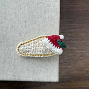 Close-up of knit Christmas hair clip with pearl detail and festive red Santa hat design
