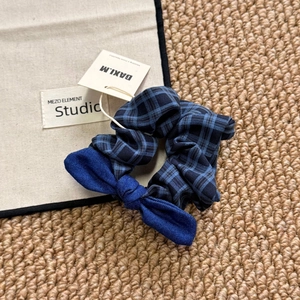 Close-up of blue plaid scrunchie with denim bow accent and brand tag on rustic fabric