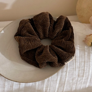 Close-up of a brown corduroy hair scrunchie with brand label on a ceramic plate