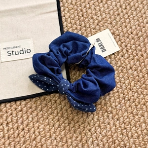 Detail of navy blue denim scrunchie with white polka dot bow on woven background