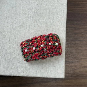 Close-up of knit Christmas hair clip with red green yarn and white pearl details
