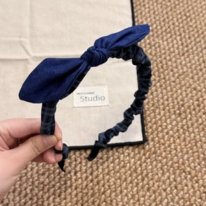 Detail view of a large navy blue denim bow headband with a checkered ruffle pattern