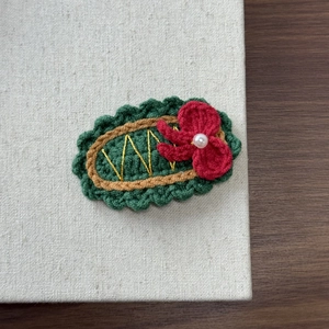 Detail of handmade crochet hair clip with a red flower and pearl on a green base