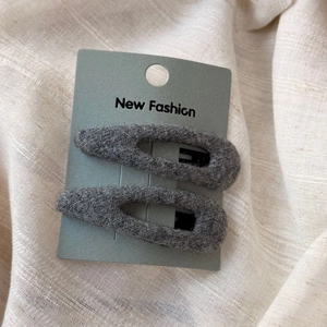 Détail macro de deux barrettes BB en velours gris sur carte de présentation