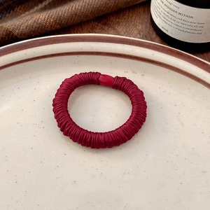 Elegant deep red pleated fabric hair tie placed on a decorative porcelain plate