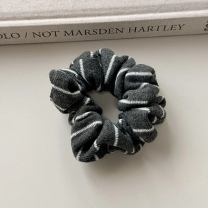 Close-up of a dark grey knitted striped scrunchie on a beige surface with soft lighting