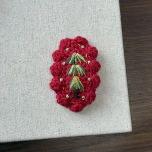 Detail of handmade crochet hair clip with green leaf embroidery and red wavy edges