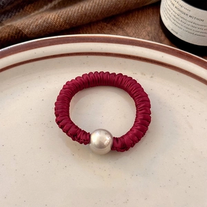 Detailed close-up of wine red satin scrunchie with large pearl bead on a ceramic dish
