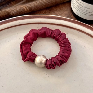 Detailed texture of burgundy satin hair scrunchie with metallic ball on ceramic tray