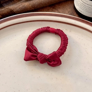 Detail of a dark red satin bow hair tie on a white ceramic plate with warm lighting