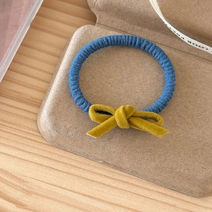 Close-up of blue high-elastic hair tie with a contrast yellow velvet bow on a rustic tray