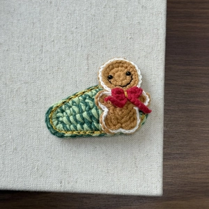 Detail of handmade knit gingerbread man hair clip with red bow and green gold-edged base