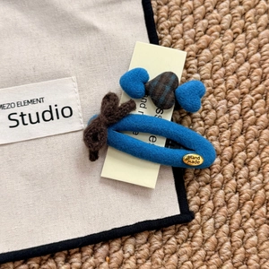 Detail of handmade blue plush flower hair clip set with brown bow and metal label