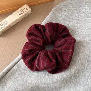 Close-up of deep burgundy knit scrunchie with grey stripes on a soft fabric background