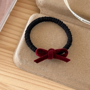 Detail of high-elasticity hair tie with a burgundy velvet bow on a brown tray