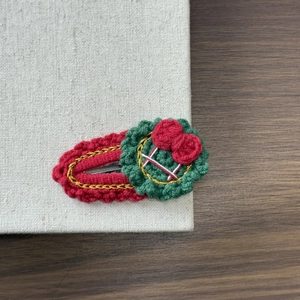 Detail of a handmade knitted Christmas wreath hair clip with red bow and gold embroidery