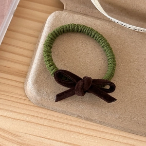 Detailed macro view of forest green knit hair tie featuring a dark brown velvet bow decoration