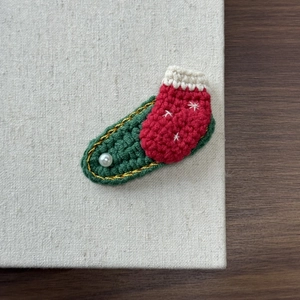 Macro detail of hand-knitted Christmas stocking hair clip with embroidery and pearl bead