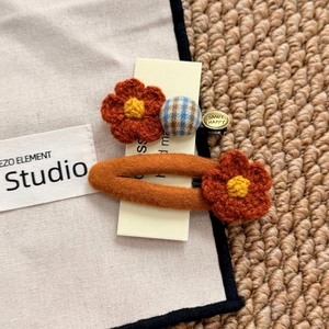 Detailed close-up of orange crochet flower hair clips with a gold smile charm on fabric