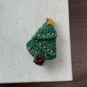 Close-up of a handmade crochet Christmas tree hair clip with golden bead decorations