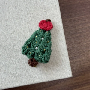 Close-up of handmade knit Christmas tree hair clip with green yarn and pearl accents