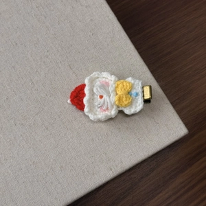 Detail of a handmade crochet Christmas hair clip with a red hat and yellow bow on metal