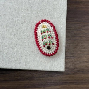 Close-up of a handmade crochet Christmas tree clip with white yarn and green embroidery