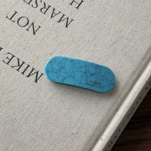 Detailed macro view of a turquoise marble acetate hair clip on a vintage fabric book cover