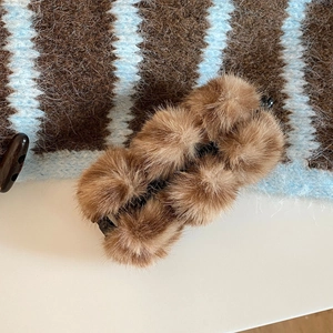 Vue détaillée de pompons en fausse fourrure marron sur une pince à cheveux noire
