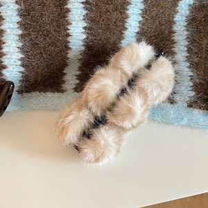Gros plan d'une pince banane en peluche beige avec plusieurs pompons en fausse fourrure