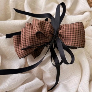 Detailed macro view of the large brown houndstooth bow hair clip and black silk ribbon detail
