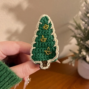Détail d'une pince à cheveux sapin de Noël tricotée main avec broderies d'étoiles jaunes