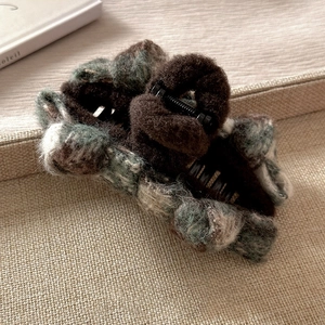 Detail of plush bow hair claw clip featuring classic plaid pattern on linen background