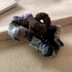 Detailed close-up of plush hair claw clip featuring brown fur and plaid fabric accents