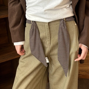 Detail of high waist green trousers with black and white striped fabric waist tie detail