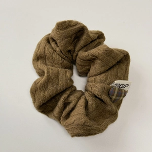 Close-up of brown knit scrunchie with plaid heart charm and dew label detail