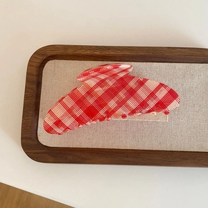 Macro detail of red plaid pattern hair claw clip on a rustic wooden display tray